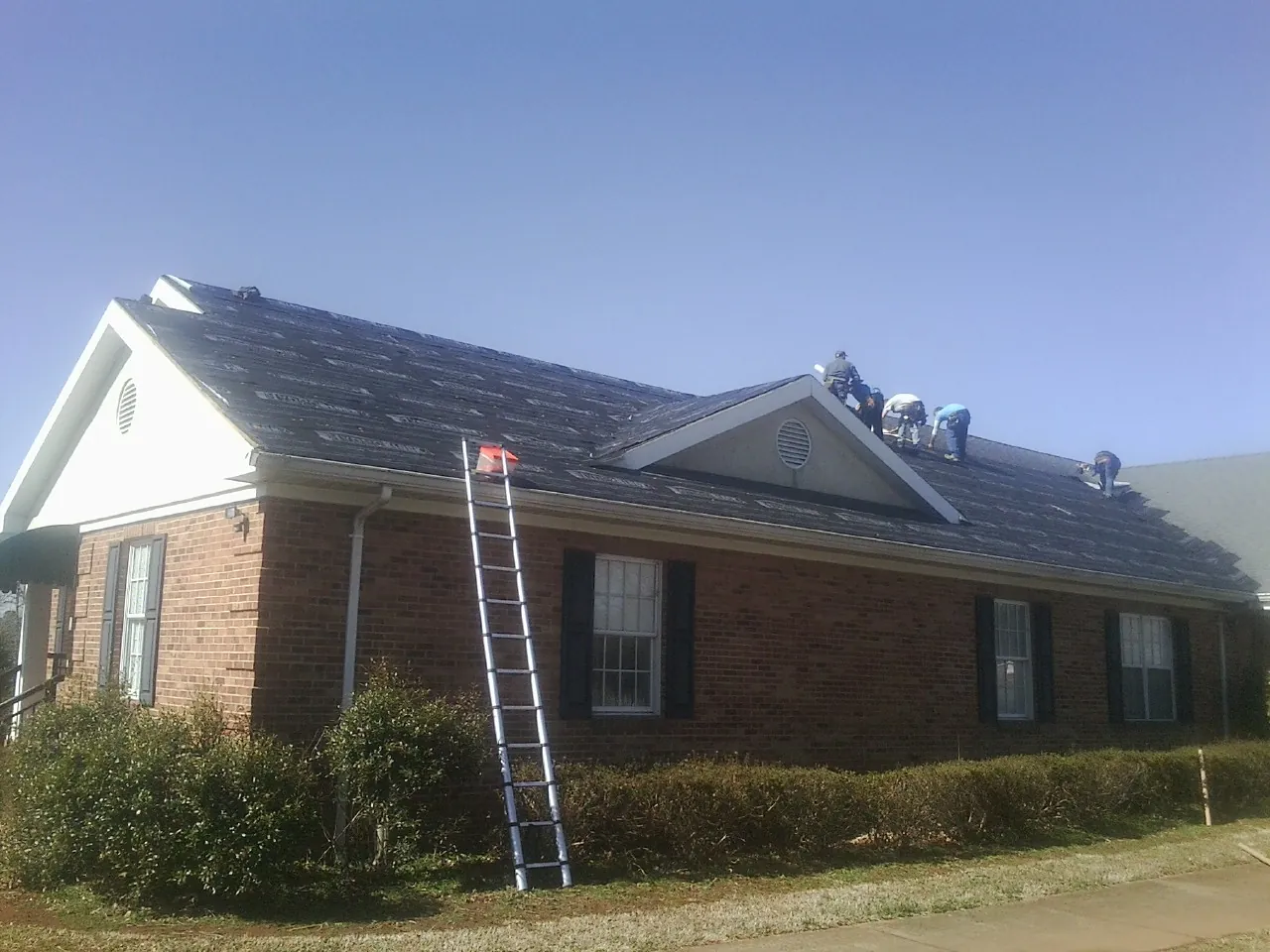 Crew tearing shingles off a brick ranch roof with a ladder set — Emergency Roof Repair work by our crew in Hoagland