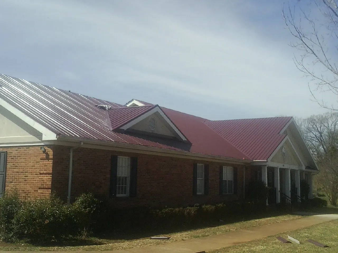 Red metal roof with gabled entries on a long brick building, from a Hail Damage Roof Repair job in Hoagland