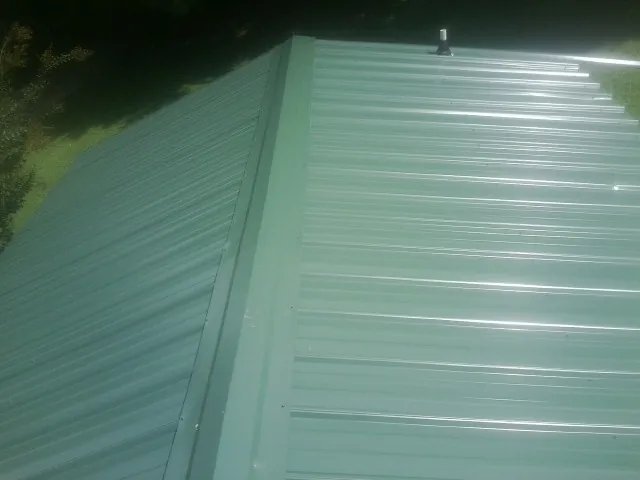 New green metal panels meeting at the ridge of a roof — Flat Roof Repair work by our crew in Hoagland