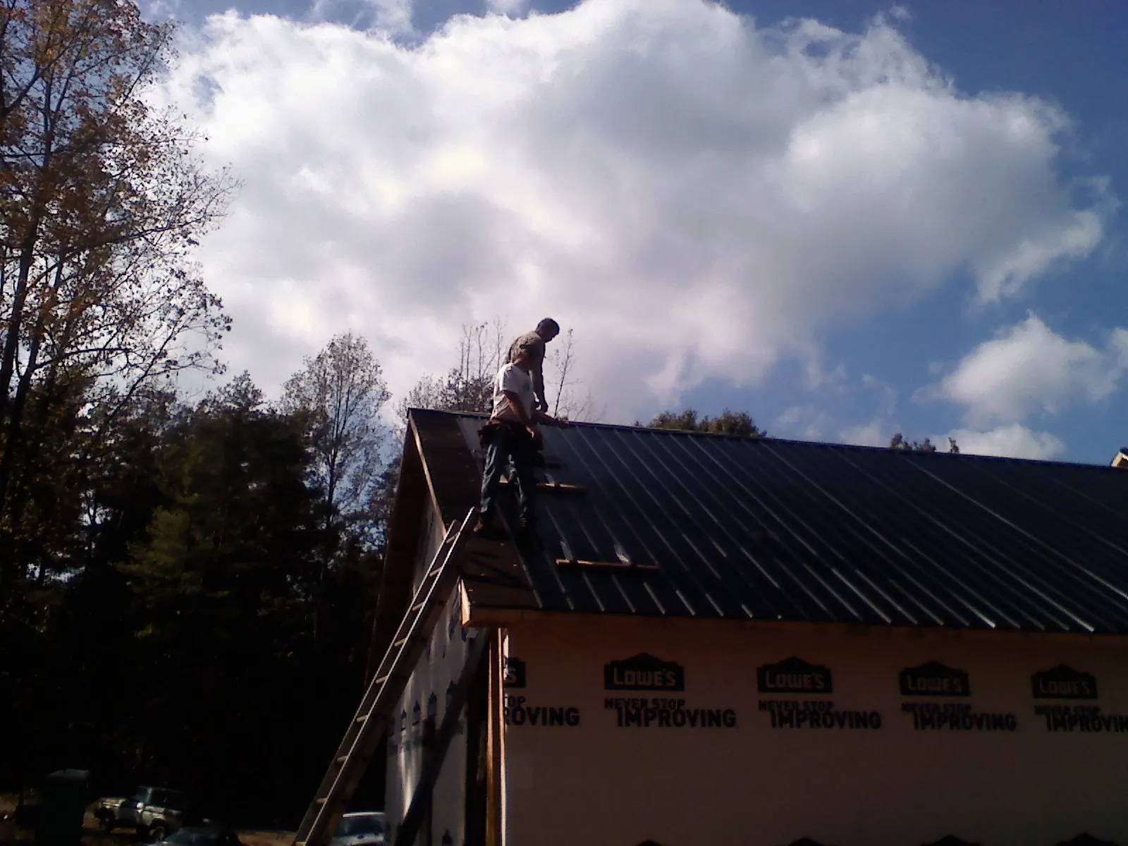Roofer fastening dark metal panels high against a cloudy sky, from a Roof Inspection job in Hoagland