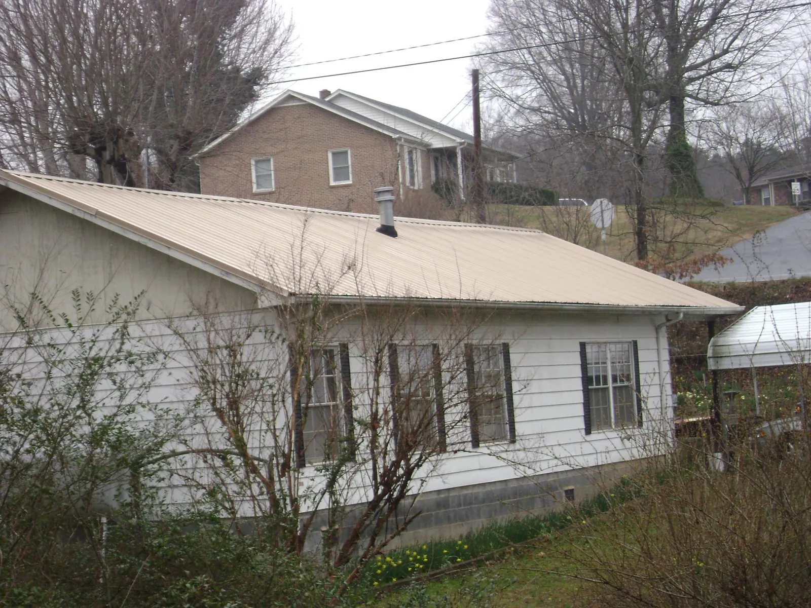 Tan metal roof on a white sided house set into a hillside — Commercial Roofing by Roofing Brothers in Hoagland